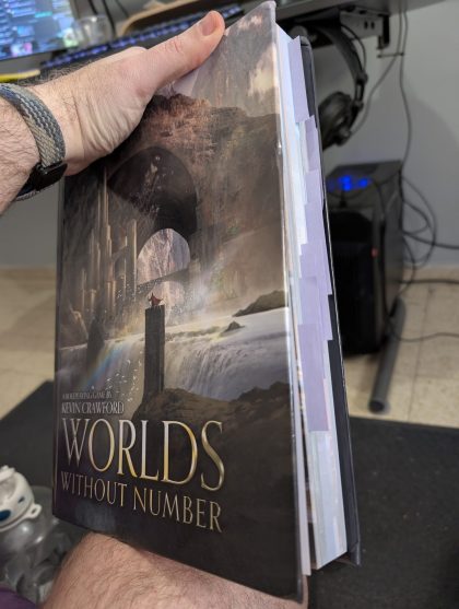 PXL_20250313_131408998.RAW-01.COVER The tabletop roleplaying game book "WORLDS WITHOUT NUMBER" by Kevin Crawford. The book has a fantasy cover featuring ancient ruins with stone arches, a waterfall, and a small figure standing on a pillar. The edge of the book shows tabbed dividers.